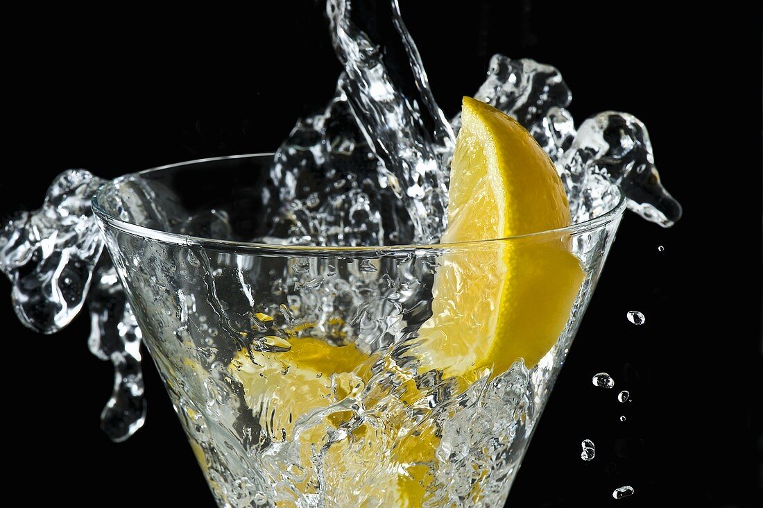 Sodawasser spritzt in Glas mit Zitronenschnitzen