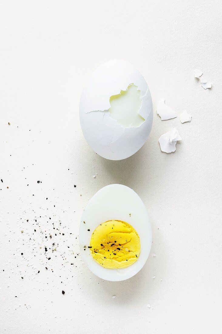 Halbes gekochtes Ei mit Pfeffer und teilweise geschältes hartes Ei