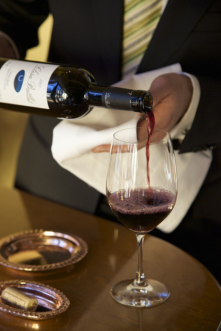 Kellner schenkt Rotwein in Glas ein