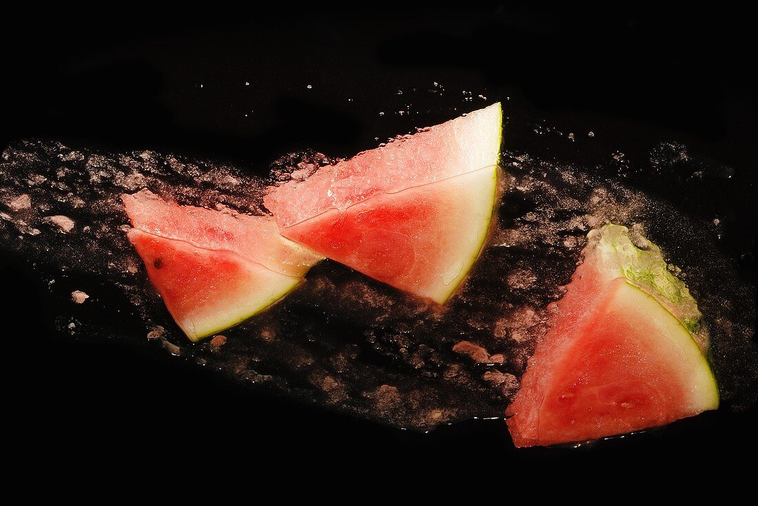 Wassermelonenstücke schlittern über schwarzen Hintergrund