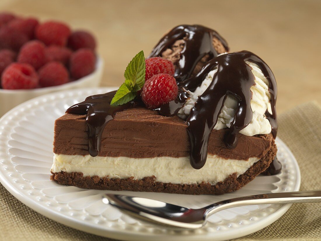Slice of Layered Ice Cream and Cheese Cake Topped with Two Scoops of Ice Cream and Chocolate Sauce