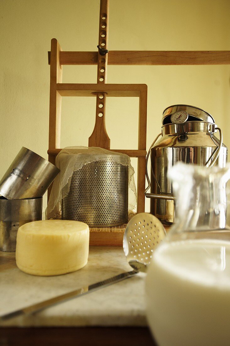 Utensilien für die Käseherstellung: Holzpresse, Formen, Käse, Milch