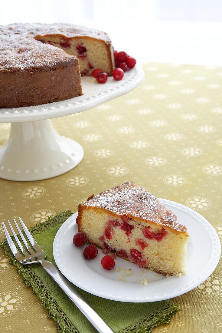 Slice of Cranberry Cornmeal Cake on a Plate; Cake on Cake Stand in Background