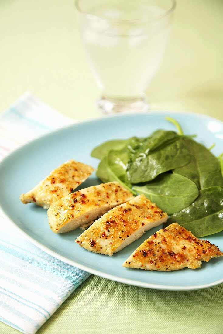 Sliced Seasoned Chicken Breast with Baby Spinach on a Blue Plate