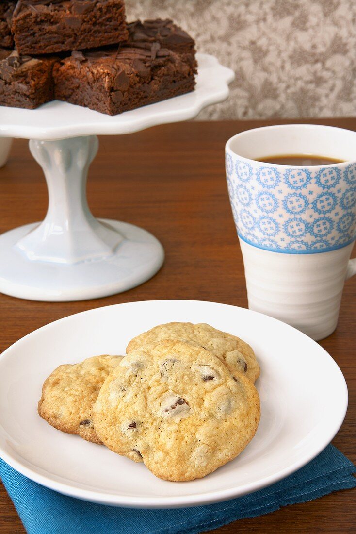 Chocolatechip Cookies auf Teller, Brownies auf Tortenständer, Kaffeebecher