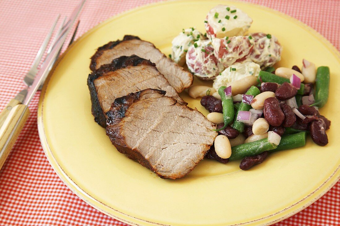 Roast Pork Slices with Bean Salad and Potato Salad on a Plate
