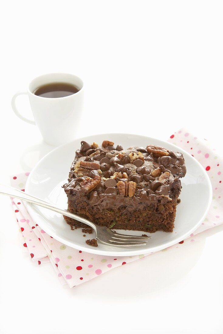 A piece of chocolate courgette cake with chocolate chips and walnut icing and a cup of coffee