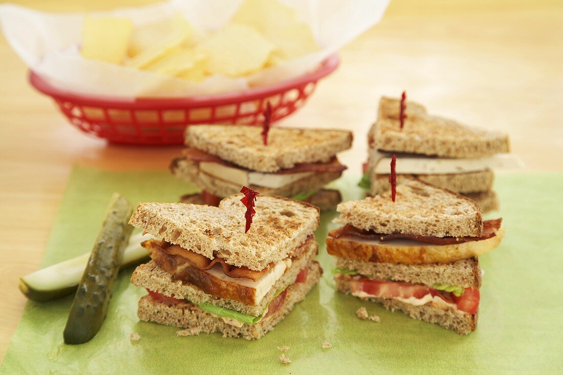 Club Sandwich Wedges with Toothpicks on Cutting Board; Pickles; Basket of Chips