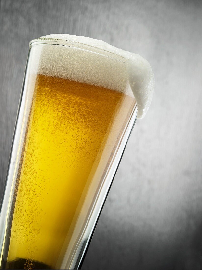 Ein Glas helles Bier mit überfliessendem Schaum