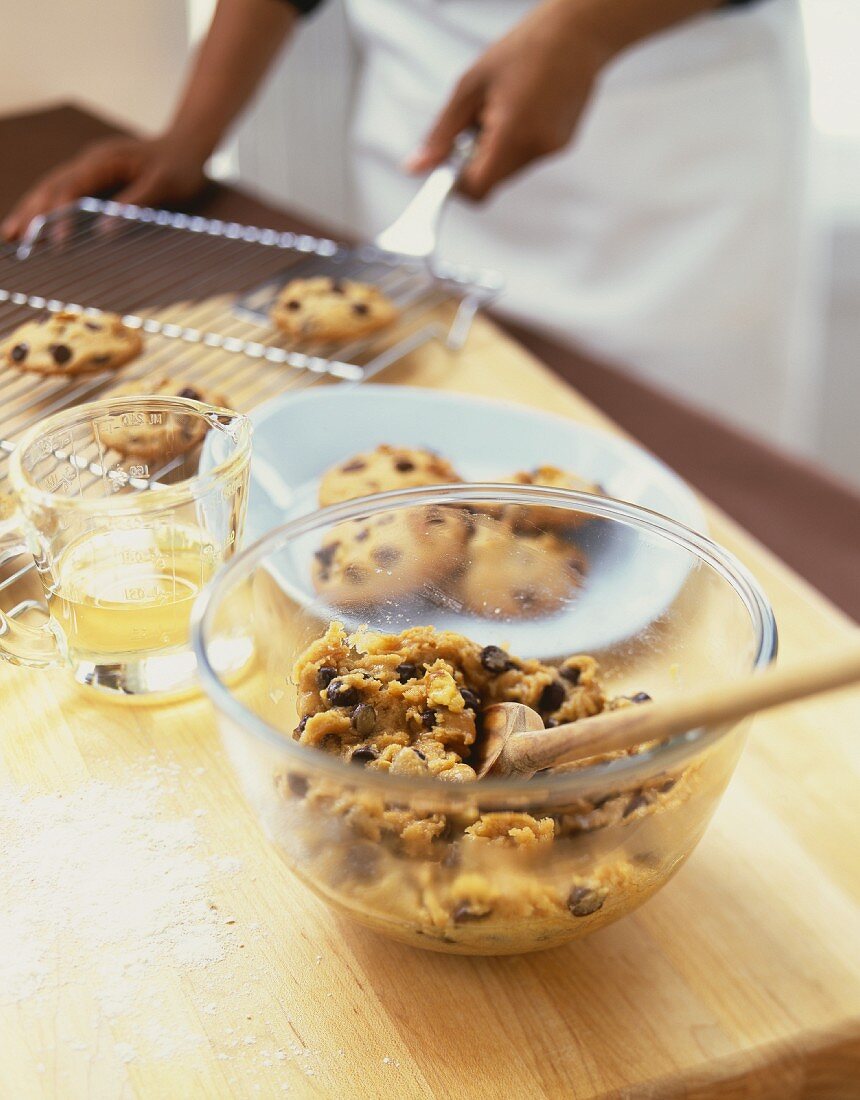 Teig für Chocolatechip Cookies in Schüssel, Person hebt Cookies vom Kuchengitter