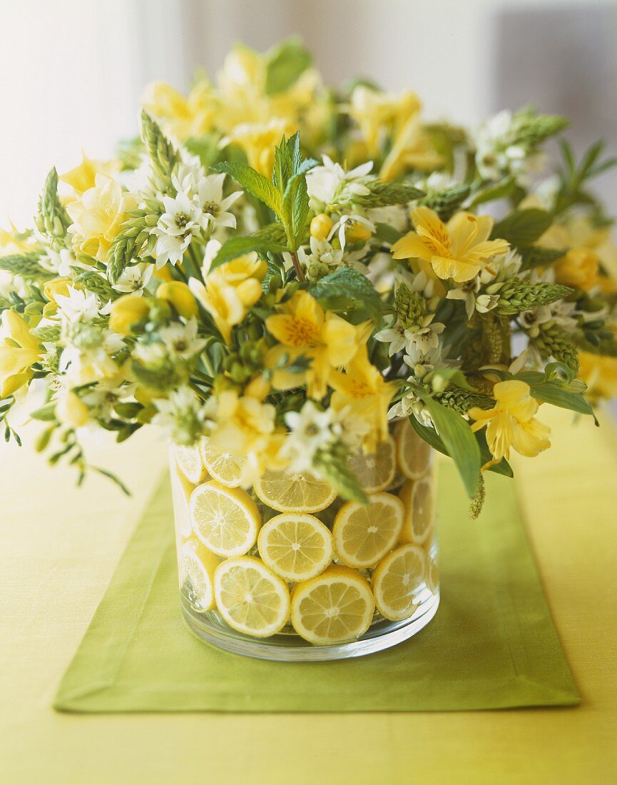 Frühlingsblumenstrauss mit Zitronen in Glasvase