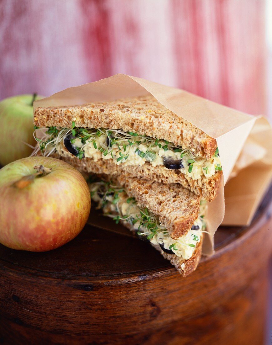 Egg Salad Sandwich with Sprouts on Wheat Bread; Wrapped in Paper with an Apple