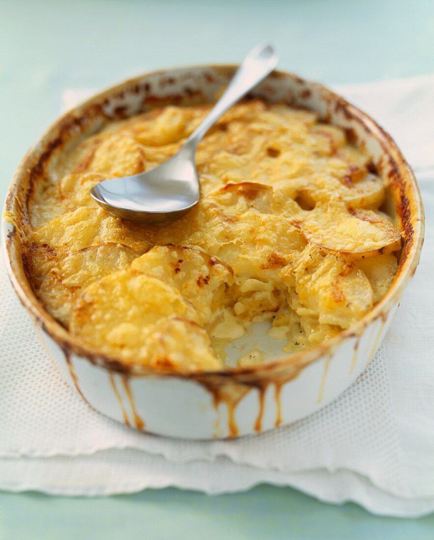 Garlic Potato Gratin in a Baking Dish with a Scoop Removed; Serving Spoon