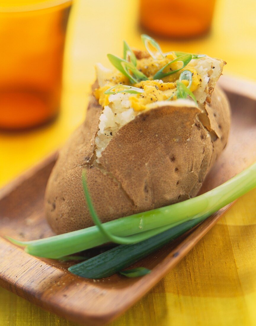 A Baked Potato with Green Onion on a Wooden Dish