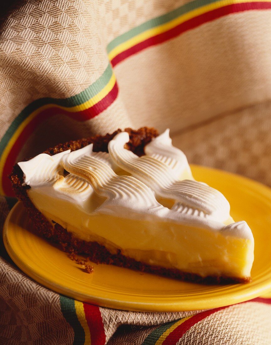 A slice on lemon meringue pie on a yellow plate