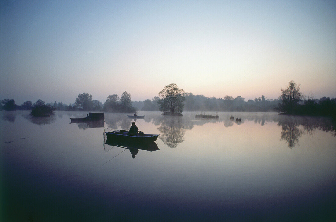 Fisherman in fishing boat at dawn, Weitmannsee Lake, Bavaria, Germany