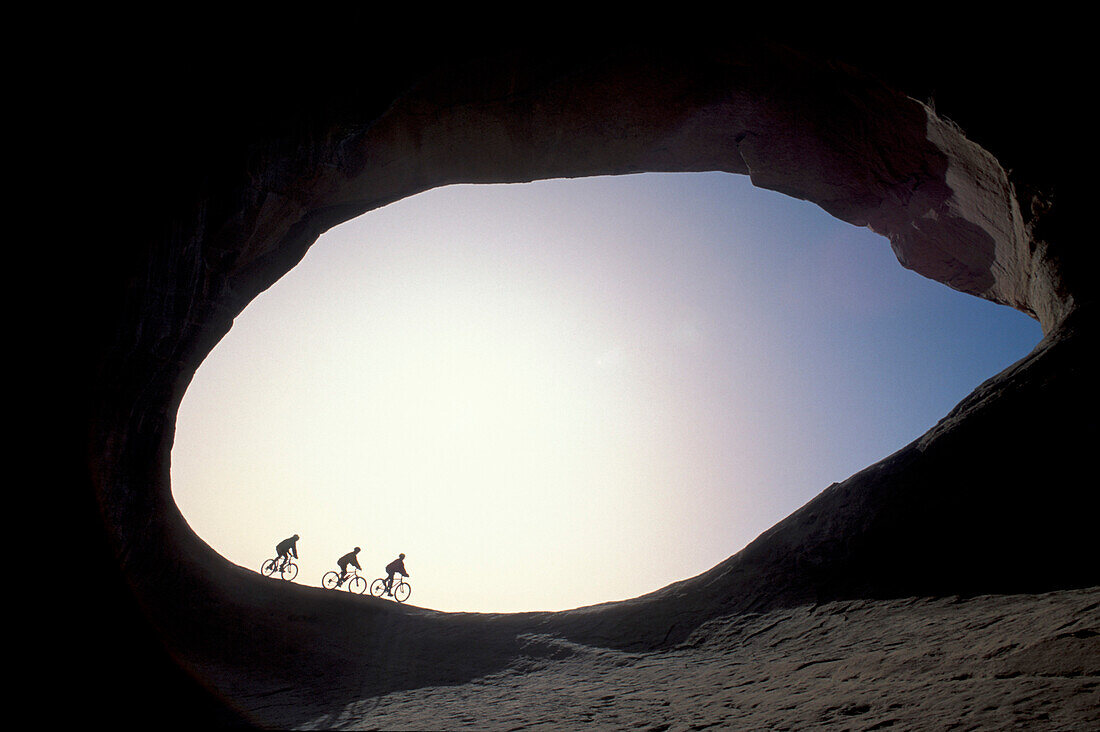 Three cyclists cycling in among rock formations, Moab, Utah, USA