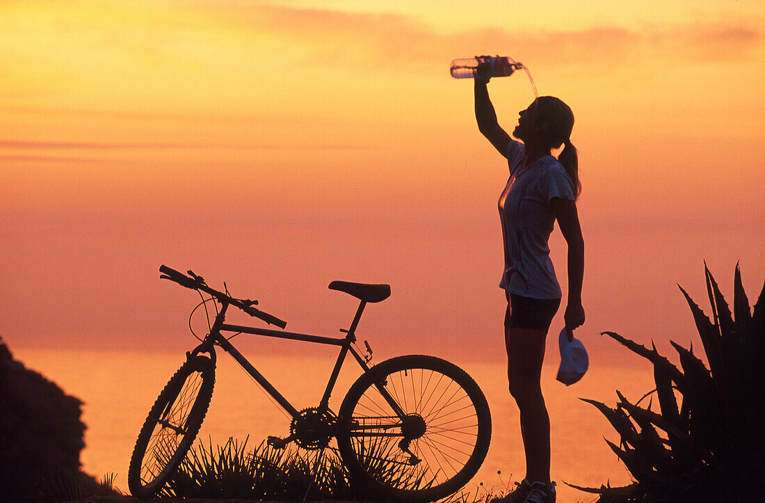 Mountainbikerin kühlt sich nach Fahrradtour mit Wasser ab, Küste, Mallorca, Spanien