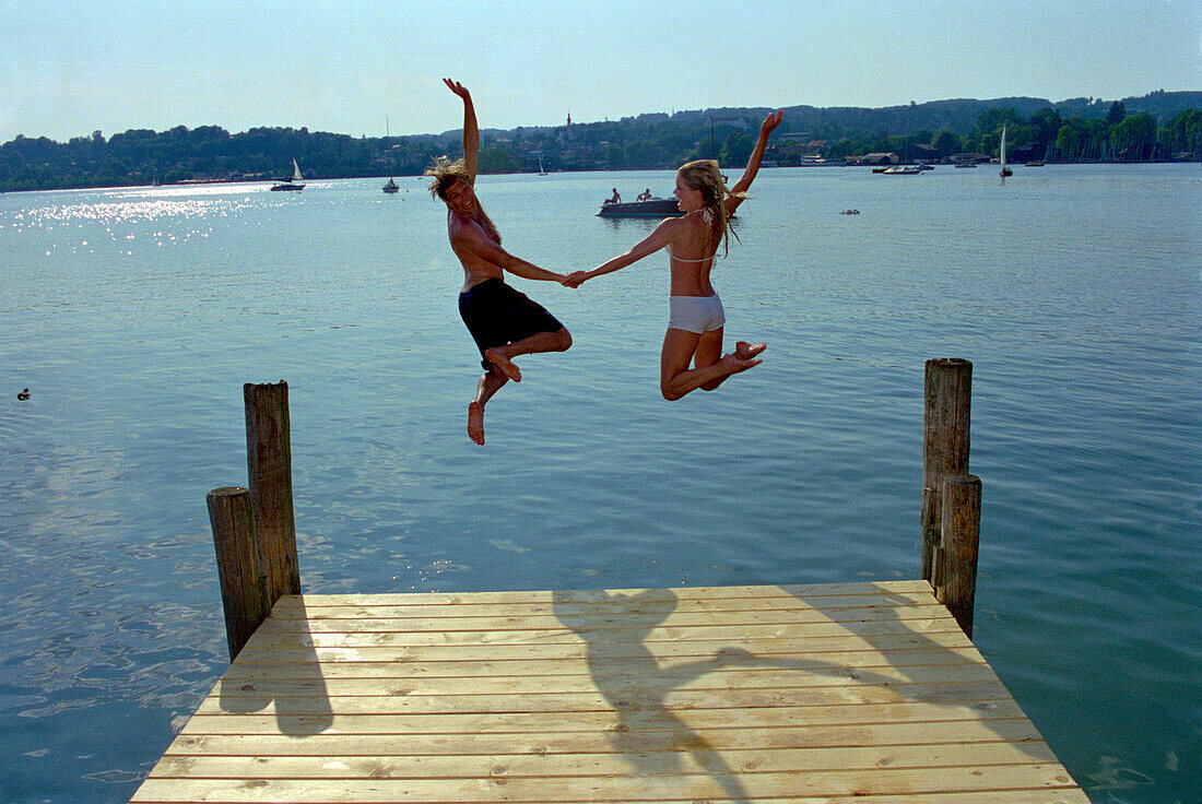 Young couple jumping from a jetty, Starnberger See, Bavaria, Germany