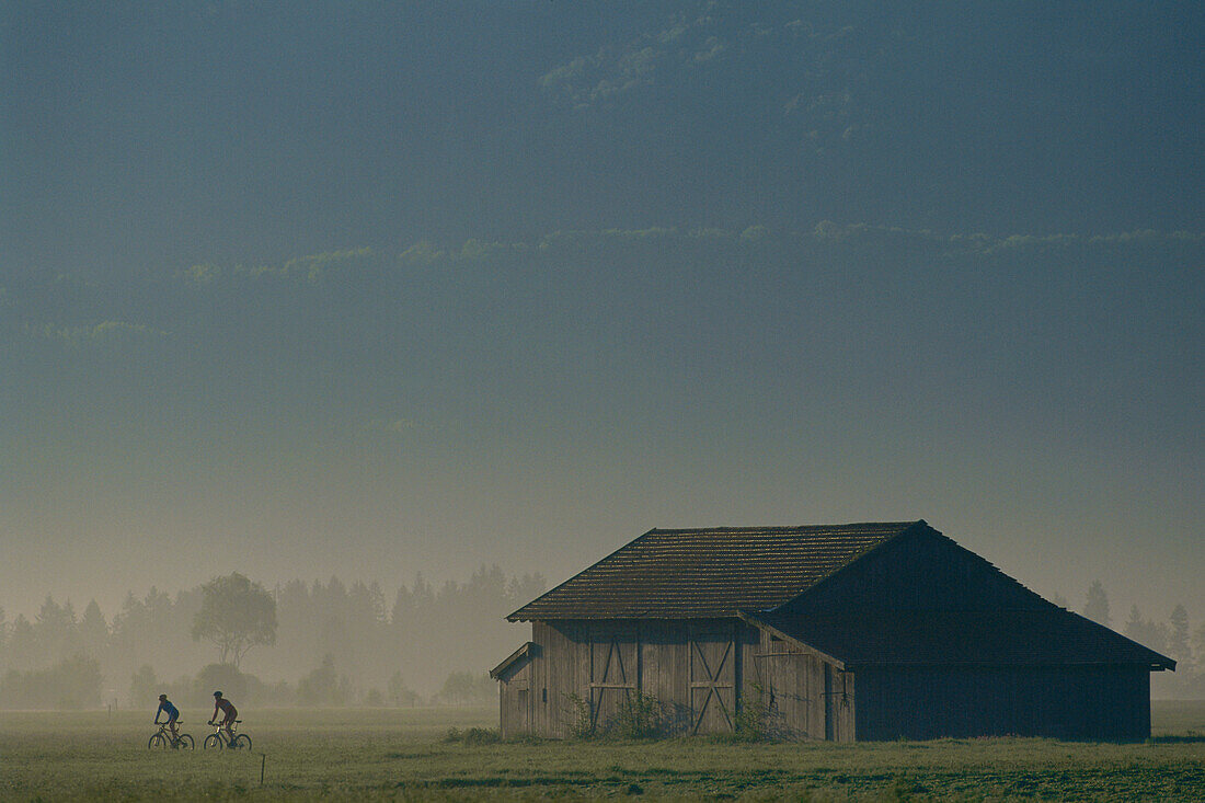 Zwei Mountainbiker neben Scheune, Fünfseenland, Oberbayern, Bayern, Deutschland