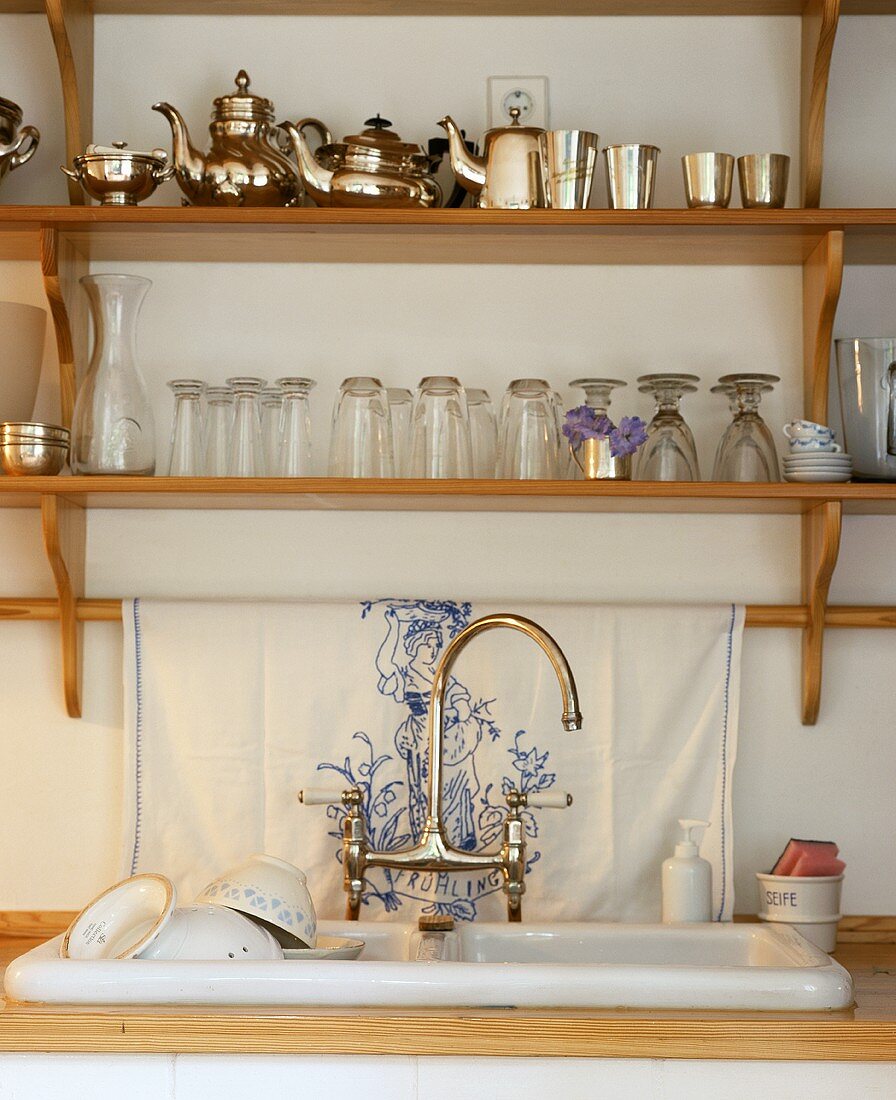 A sink with a wooden shelf filled with glasses and silverware