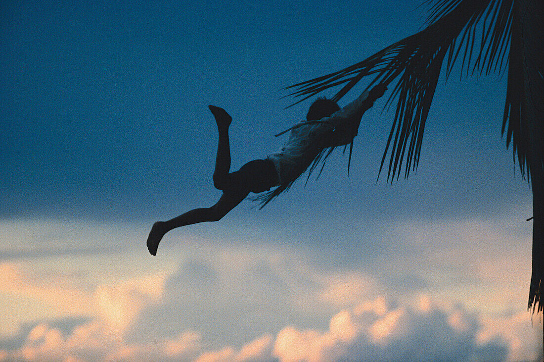 Junge hängt an Palmenblatt, Karibik