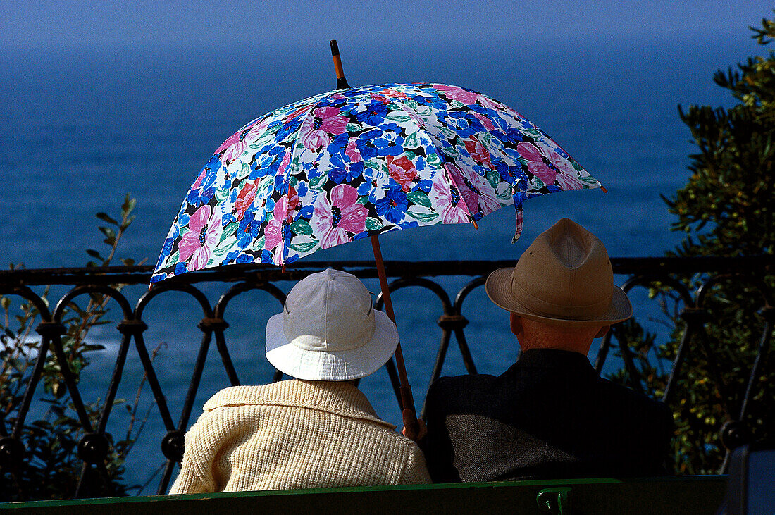 Rentnerpaar auf Bank, mit Sonnenschirm