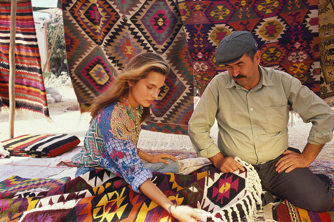 Touristin und Verkäufer an einem Marktstand mit Teppichen, Bodrum, Türkei, Europa