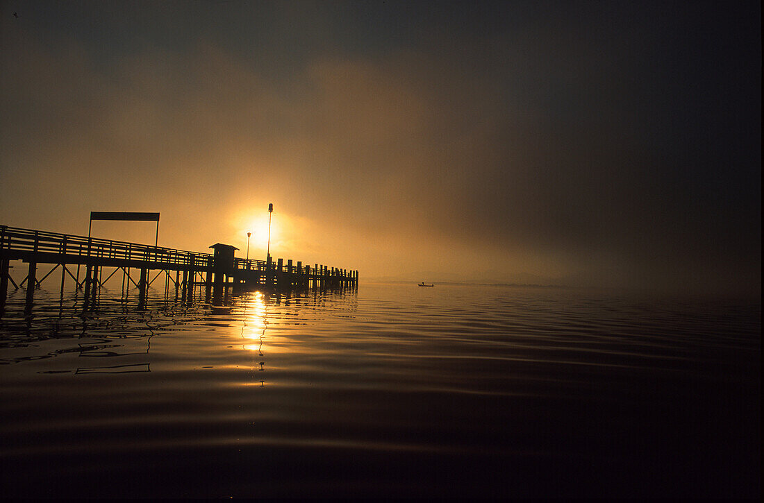 Ein Holzsteg auf dem Chiemsee bei Sonnenuntergang, Bayern, Deutschland