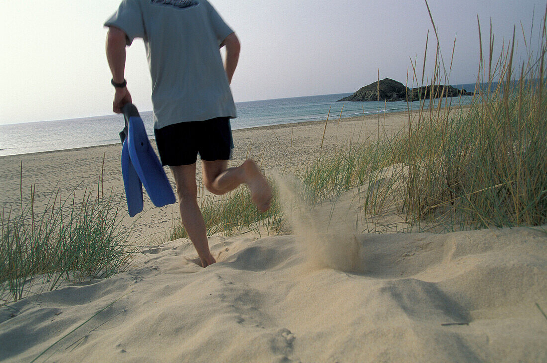 Mann läuft mit Taucherbrille und Taucherflossen ans Meer, Chia, Costa del Sud, Sardinien, Italien