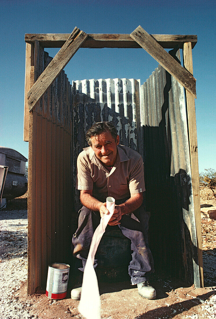 Opal miner on outdoor shed toilet, outback, Australia