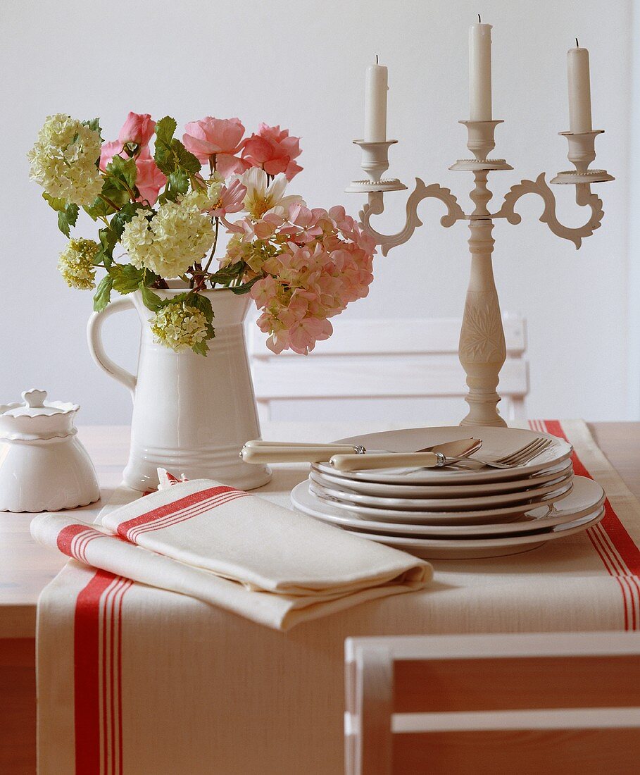 A bunch of flowers in a jug, a candle holder and plates