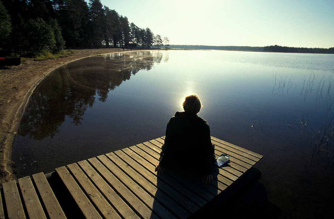 Person sitting on jetty at Suomunjaervi, Patvinsuo National Park, Karelia, Finland
