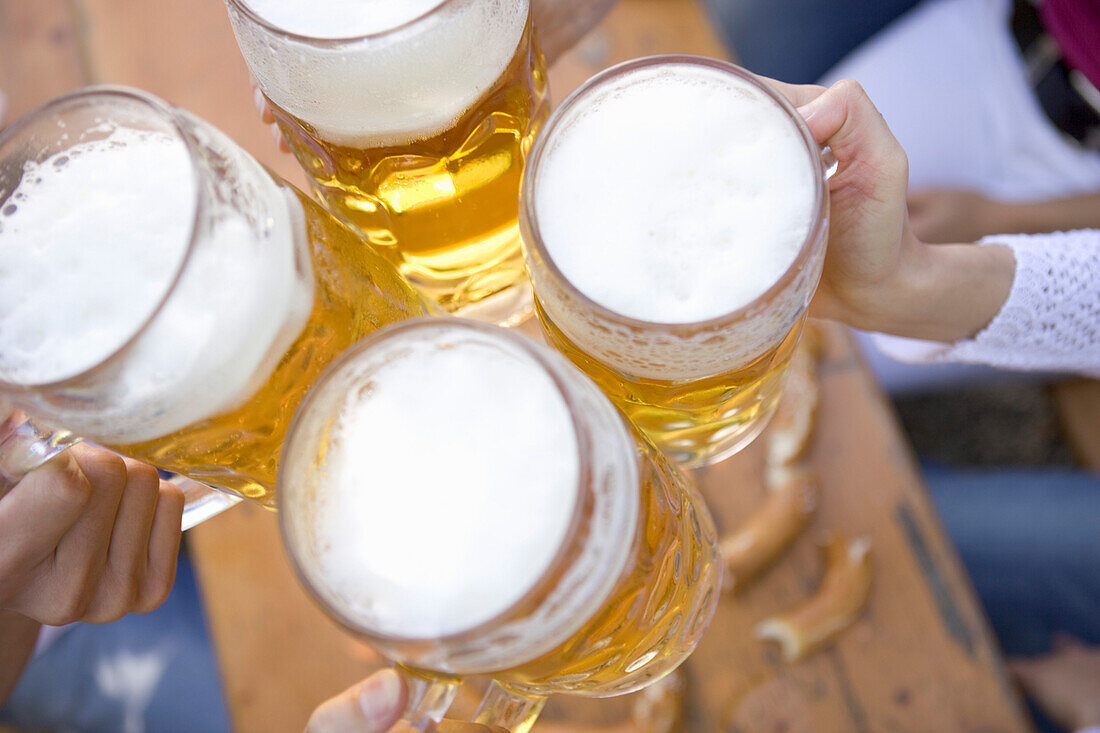Four hands toasting with beer steins above table, Munich, Bavaria