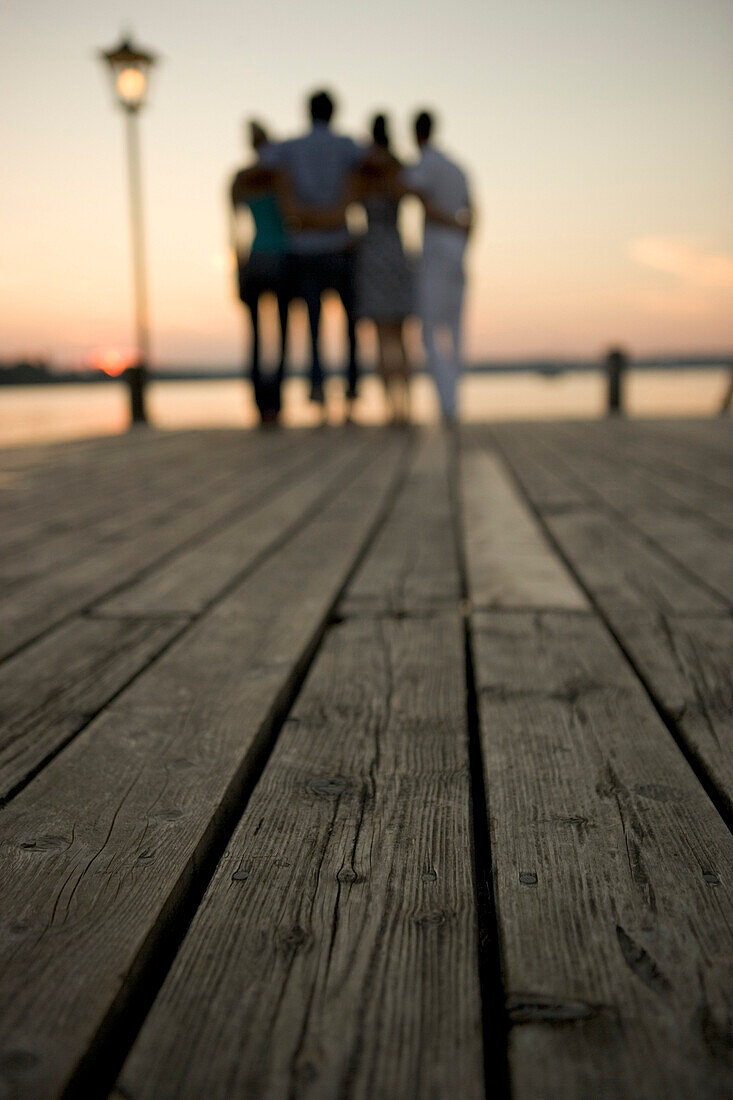 Four young people standing on boardwalk at sunset, Munich, Bavaria