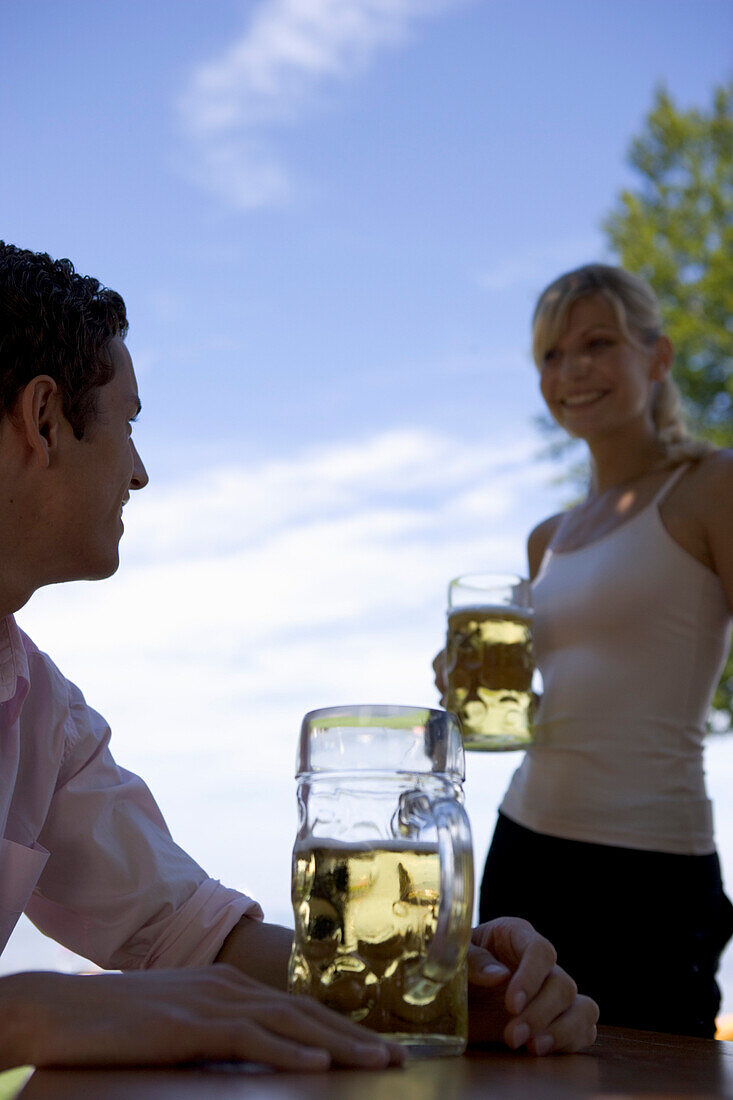 Zwei junge Erwachsene treffen sich in Biergarten beim Starnberger See, Bayern, Deutschland