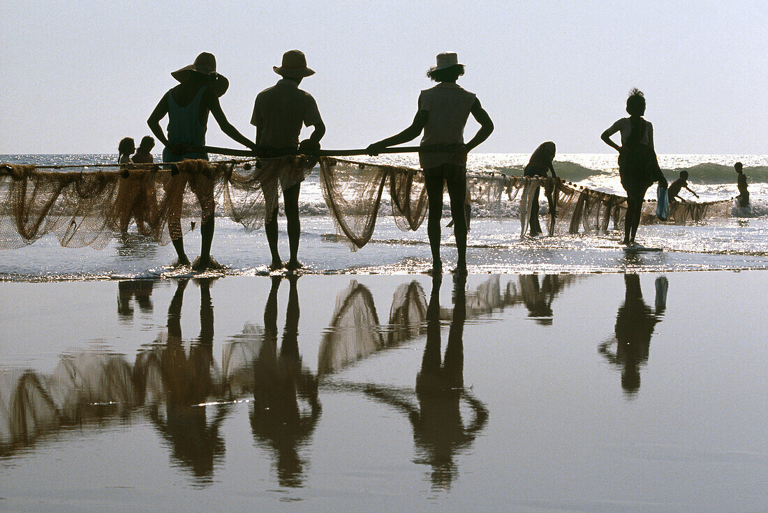 Fischer ziehen bei Sonnenuntergang ein Netz an den Strand, Baga Strand, Goa, Indien