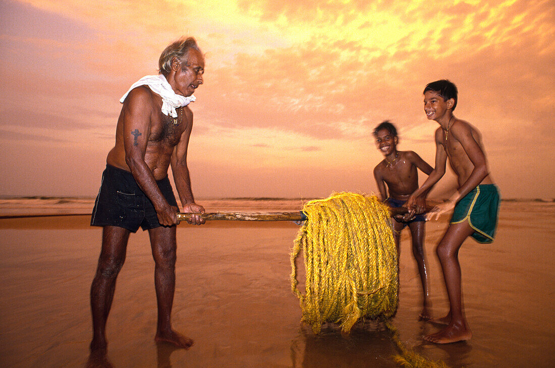 Fishermen carrying a rolled up rope at the beach at sunset, Calangute Beach, Goa, India