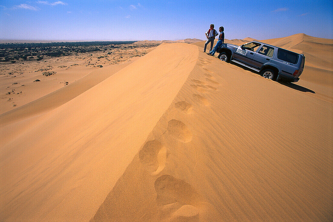 Menschen und Geländewagen auf einer Düne im Sonnenlicht, Namibia, Afrika