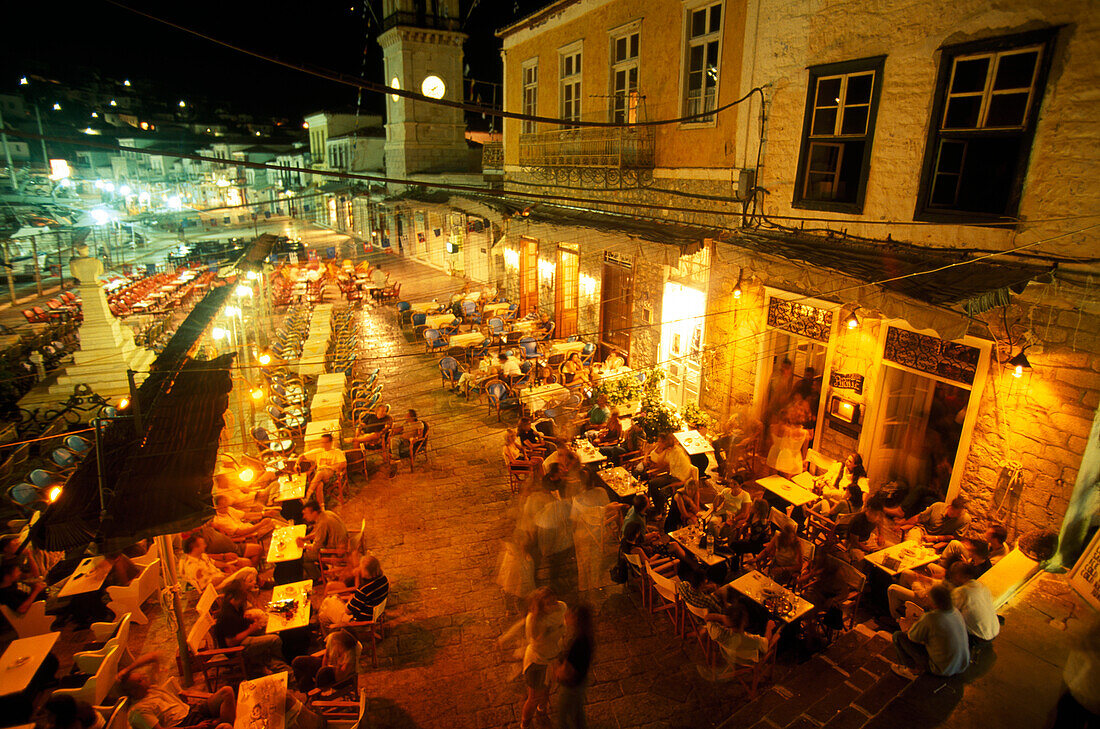 Menschen sitzen nachts vor einer Bar auf der Promenade, Hydra, Saronische Inseln, Griechenland
