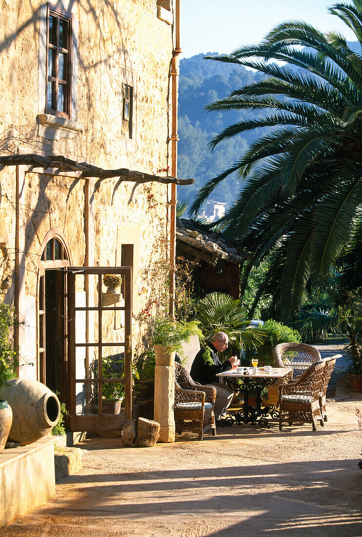 A man having breakfast on the terrace of Finca Hotel de Reis in the sunlight, Valle de los Naranjos, Soller, Majorca, Spain