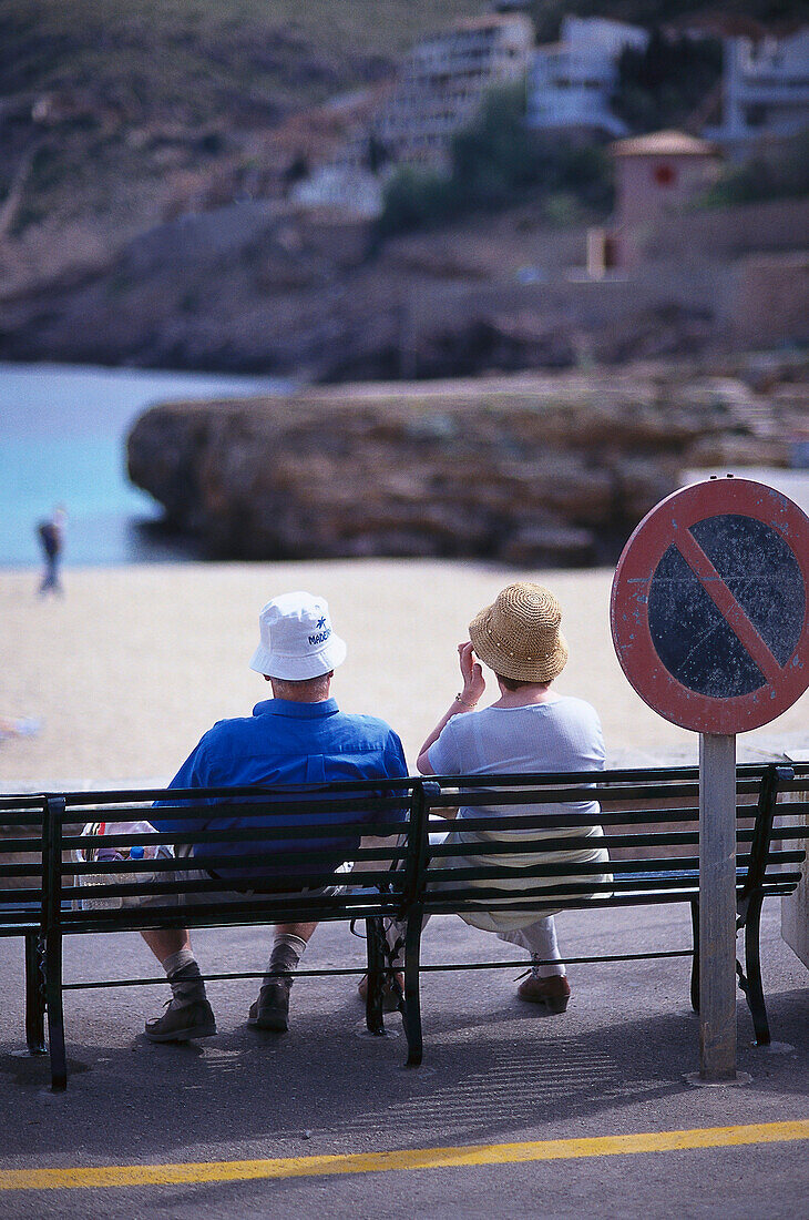 Senior couple sitting on bench, Cala Molins, Cala se Sant Vicenc, Majorca, Spain