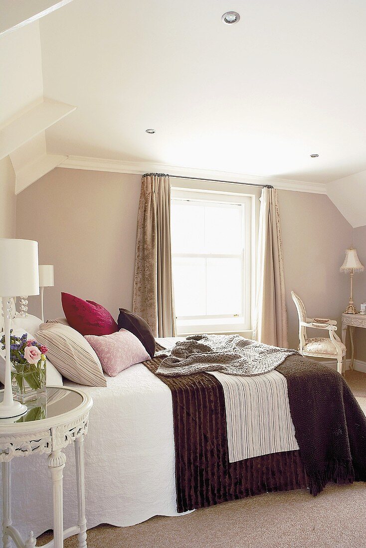 A cosy attic bedroom with a pile of cushions on the bed