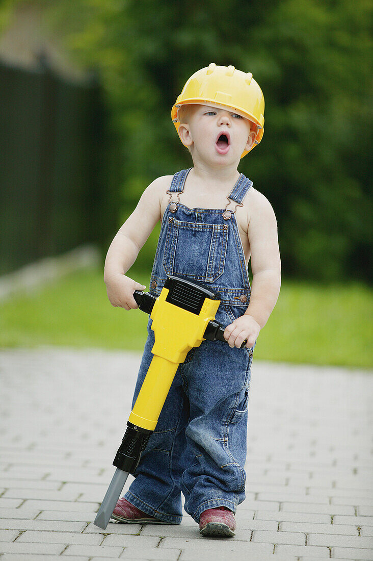 Boy 3-4 years, wearing hard hat holiding toy jackhammer, Styria, Austria