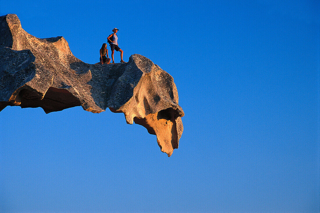Two hikers on a rock ledge at Capo d´Orso, a bear shaped rock, Sardinia, Italy