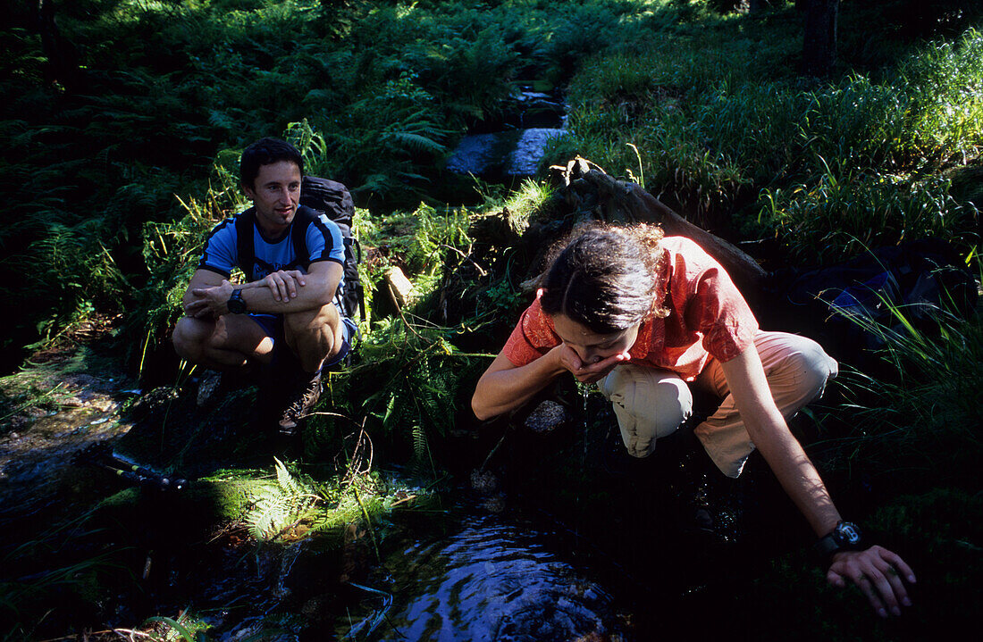 Hiking couple resting and drinking water at creek, Boehmerwald, Muehlviertel, Upper Austria