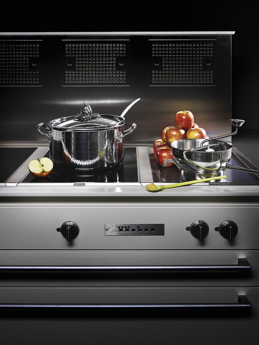 A pot and kitchen utensils on a cooker with a chrome extractor hood