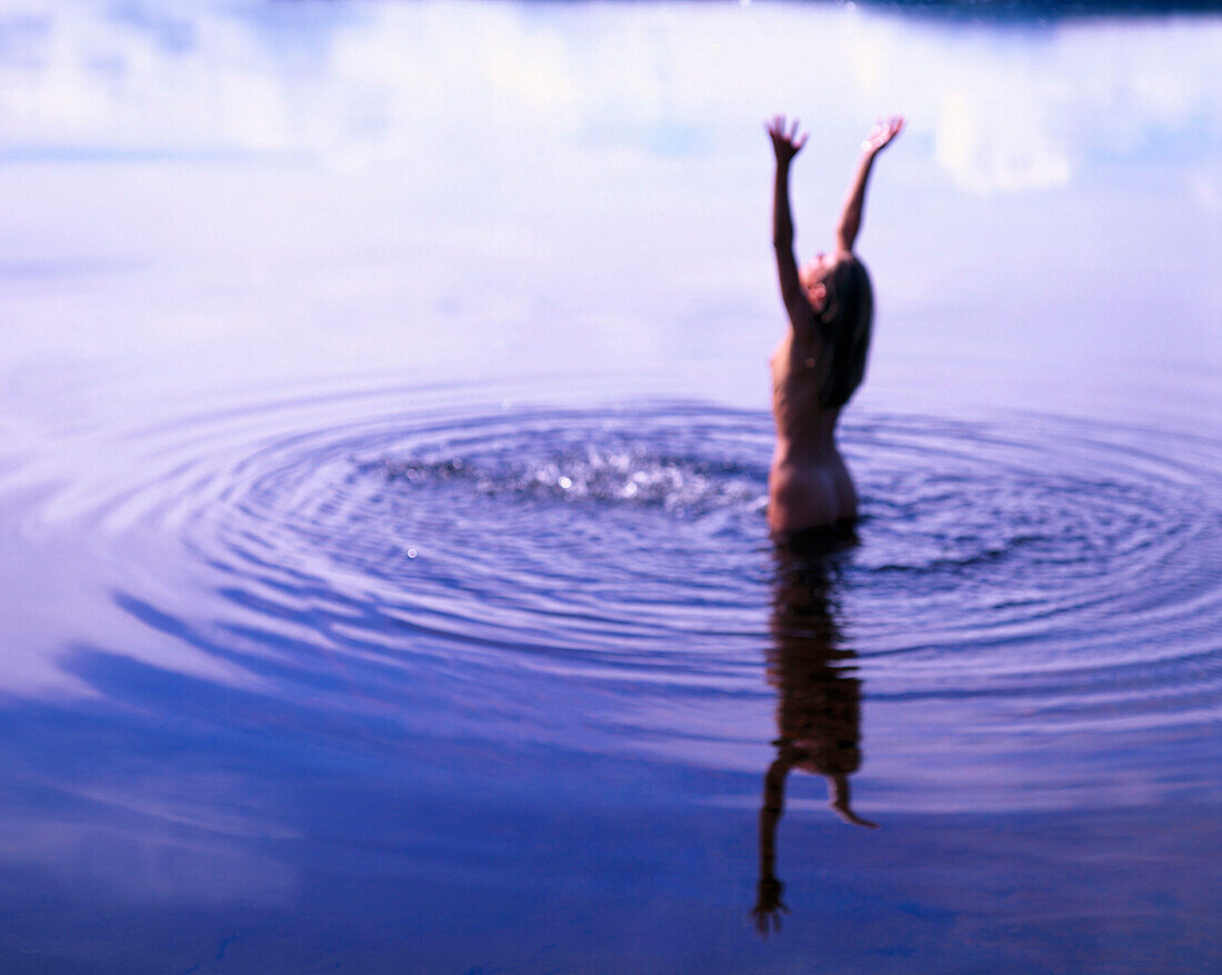 Woman standing in a lake, arms raised high, Sweden