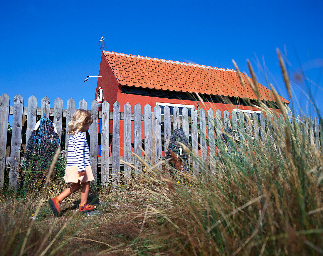 Little girl walking along fence and small house, Bornholm, Baltic Sea, Denmark