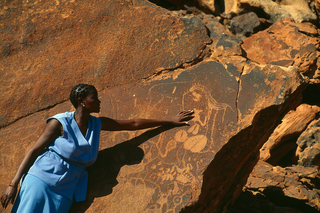 Female tour guide showing stone carvings, Petroglyphen, Damara Tourguide, Twyfelfontein, Damaraland, Namibia, Africa